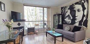 Una sala de estar con una mesa de centro de vidrio, un sofá gris, un televisor y un cuadro grande en la pared.