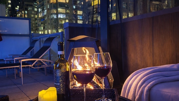 Een terras op het dak met een fles wijn, twee wijnglazen en een kaars op een dienblad.