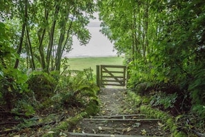 Stroll through lush greenery to a serene entrance, surrounded by nature and a tranquil body of water.