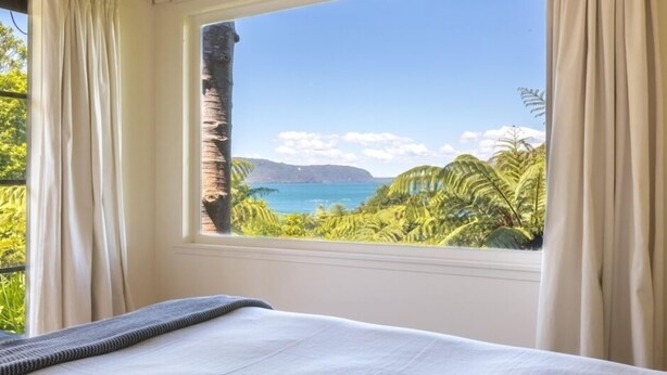 Un dormitorio con un ventanal que ofrece vistas a un paisaje tropical y al océano.