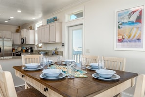 Un coin repas avec une table en bois dressée pour six personnes, entourée de chaises blanches.