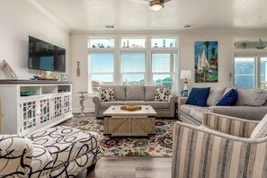 A living room with a TV, a sofa, a coffee table, and a view of the outside.