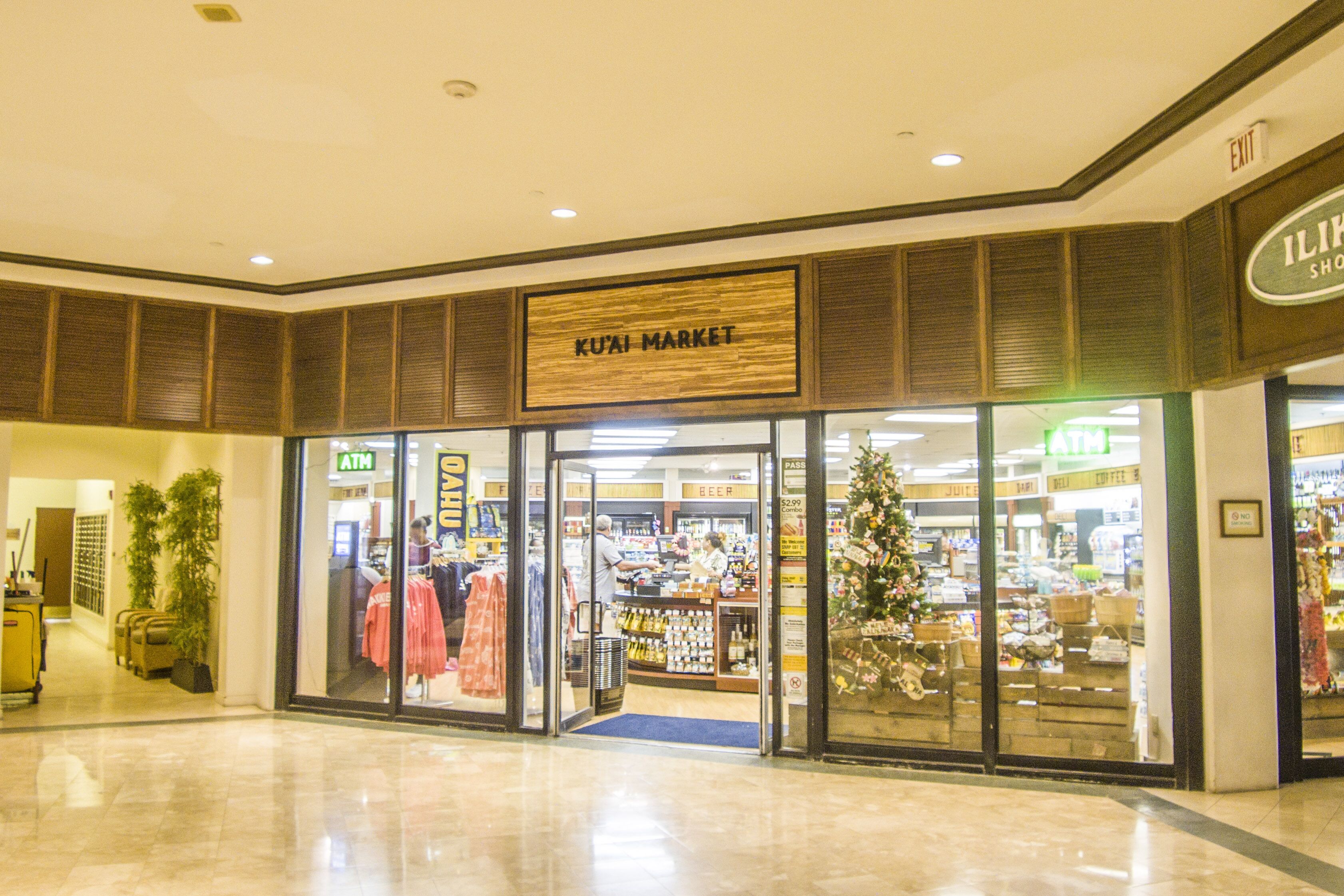 Un centro comercial con un letrero 'KUAI MARKET', un cajero automático y un árbol de Navidad.