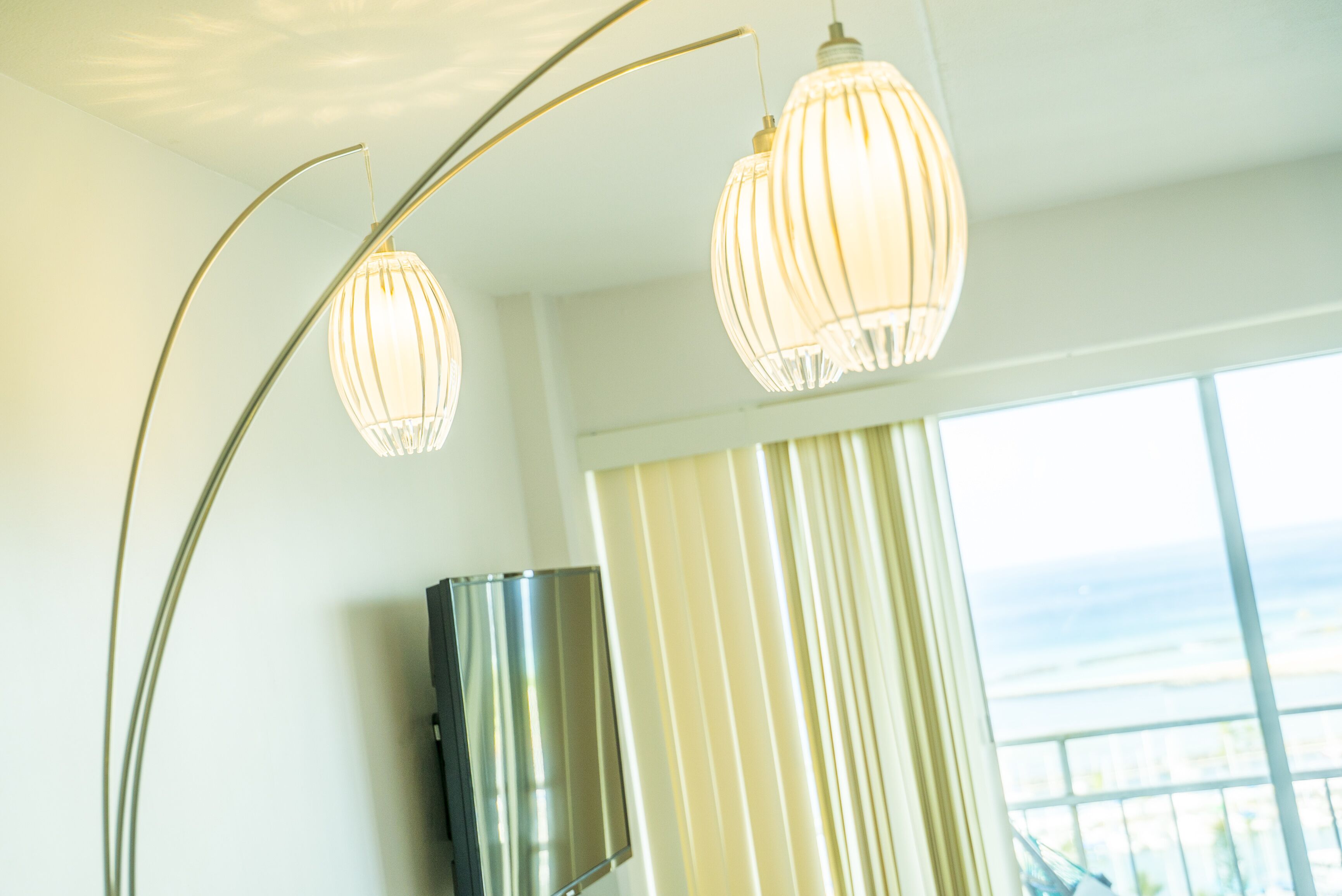A room with a large window, a flat-screen TV mounted on the wall, and two pendant lights with a ribbed design.