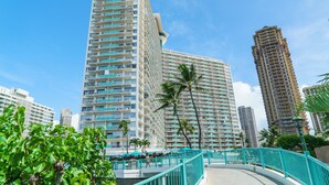 Un hôtel de grande hauteur doté de nombreux balcons, d’une promenade turquoise aux lignes courbes et de palmiers.