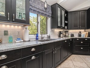 A modern kitchen with dark cabinetry, a granite countertop, and a window with a patterned valance.