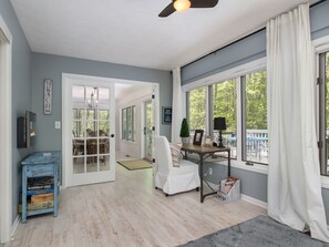 A spacious room with a large window, a ceiling fan, and a dining area visible through an open door.