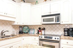 A kitchen with white cabinets, a microwave, a stove, a sink, and various kitchen utensils. - Hoos at the Beach - Lovely 4 BR Sea Star Village Townhouse; Ocean View! (Surf City)