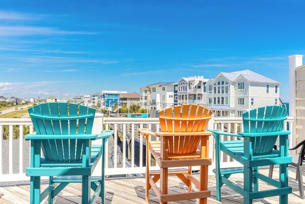 A wooden deck with two turquoise Adirondack chairs and one orange Adirondack chair.