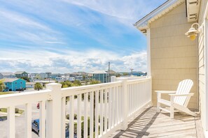A balcony with a white railing, a white chair, and a view of a residential area with houses and a clear sky. - Hoos at the Beach - Lovely 4 BR Sea Star Village Townhouse; Ocean View! (Surf City)