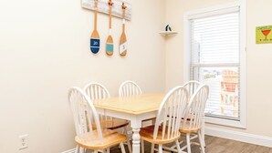 A dining area with a wooden table and white chairs, a wall-mounted number board, a window with blinds, and a small shelf with a decorative item. - Hoos at the Beach - Lovely 4 BR Sea Star Village Townhouse; Ocean View! (Surf City)