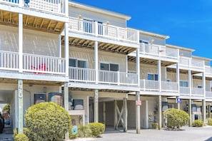 A multi-story hotel with balconies, a parking area, and a clear blue sky. - Hoos at the Beach - Lovely 4 BR Sea Star Village Townhouse; Ocean View! (Surf City)
