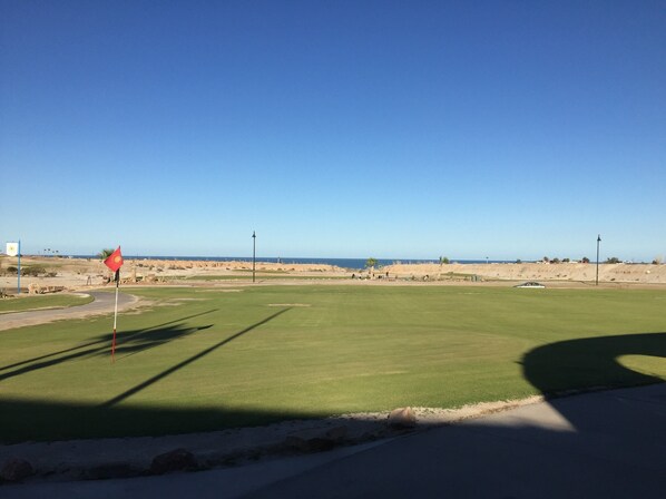 A golf course with a clear view of the ocean and a flag on the tee area.