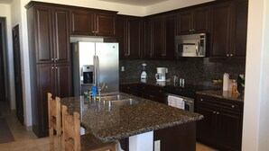A modern kitchen with dark wood cabinets, granite countertops, stainless steel appliances, and a central island with seating. - Beautiful Beach Condo with Sea Views in Beach/ Golf Resort with Wifi (San Felipe)