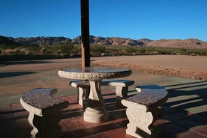 A patio area with a round table and three matching chairs, set against a backdrop of mountains. - Indian Cove Ranch, Joshua Tree on the Border of National Park-Hot Tub-Pool-WiFi (Twentynine Palms)