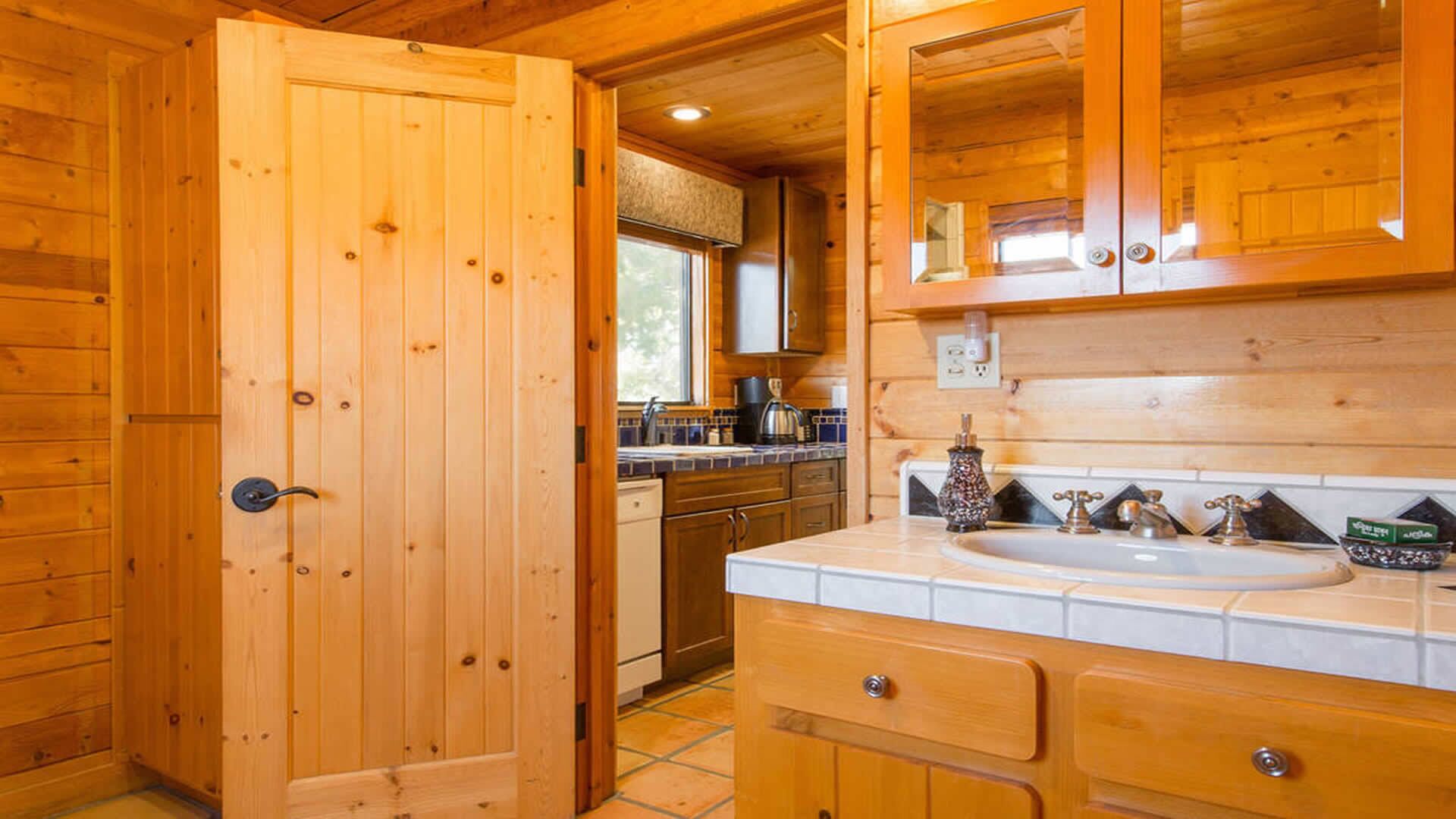 A wooden cabin interior with a kitchen area, including cabinets, a sink, and a window.