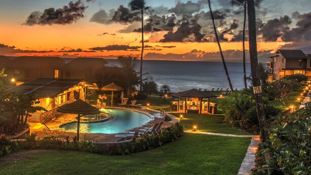 Un resort con piscina, sillas de descanso y vista al océano al atardecer.