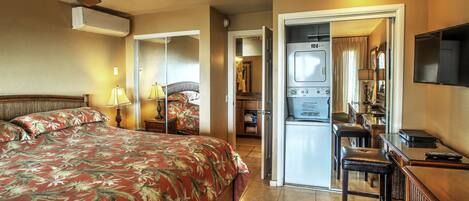 Ein Hotelzimmer mit Bett, Schreibtisch, Stuhl, Fernseher und Deckenventilator.