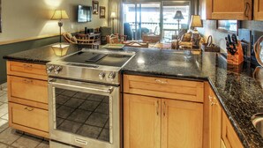 Una cocina con estufa, horno y lavaplatos integrados, armarios de madera y un comedor con sillas y mesa.