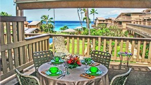Un área de comedor al aire libre techada con una mesa preparada para cuatro, con vista a una playa y al océano.