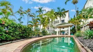A swimming pool surrounded by lush greenery and palm trees, with a covered seating area and a building in the background. - Luxury Beach Front Accommodation  (Trinity Beach)