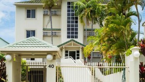 A large, multi-story building with a gated entrance, palm trees, and a covered porch. - Luxury Beach Front Accommodation  (Trinity Beach)