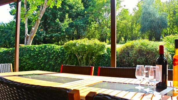 Un área de comedor al aire libre con una mesa dispuesta para dos personas, rodeada de abundante vegetación y árboles.