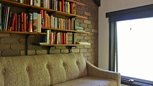 Una habitación acogedora con un sofá color beige, estanterías de madera llenas de libros y un ventanal grande.