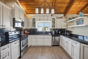 A kitchen with white cabinets, a black countertop, stainless steel appliances, and a wooden ceiling.