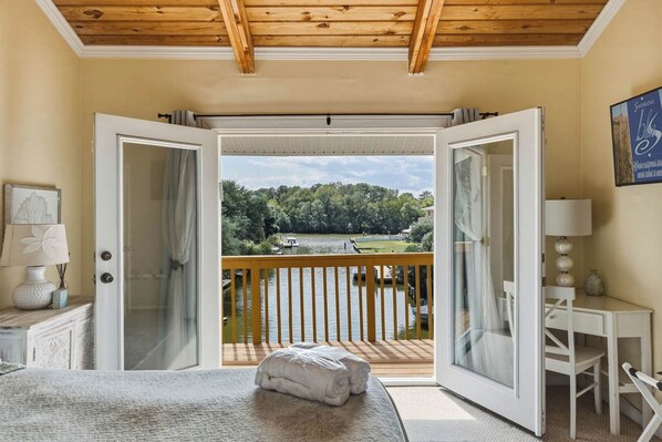 A bedroom with a bed, a desk, and a view of a lake through open doors.