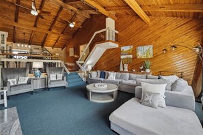 A spacious living area with a high ceiling, a staircase, and a seating arrangement.