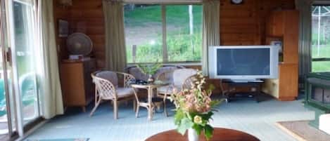 A wooden cabin interior with a dining area, a television, and a large window.