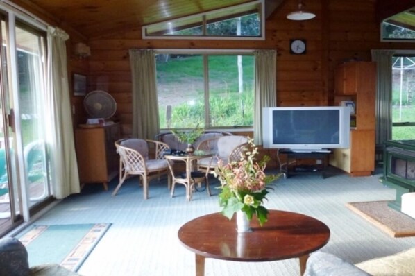 A wooden cabin interior with a dining area, a television, and a large window.