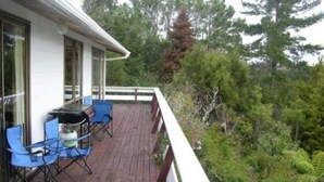 A wooden deck with blue chairs and a table, surrounded by dense forest. - Private and pet friendly lockwood house (Okiato)