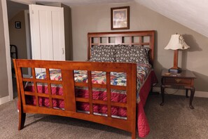 A bedroom with a wooden bed, a nightstand, a lamp, and a door.