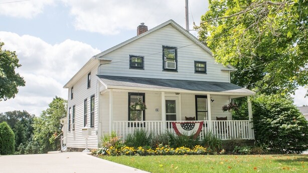 A two-story house with a front porch, a chimney, and a flag on the railing. - Geauga Maple Cottage (Chardon)