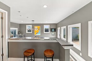 A modern kitchen with a central island, two bar stools, and a window overlooking a garden.