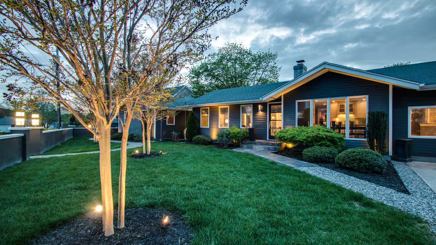 A modern house with a well-maintained lawn, a large tree, and a driveway leading to the entrance.