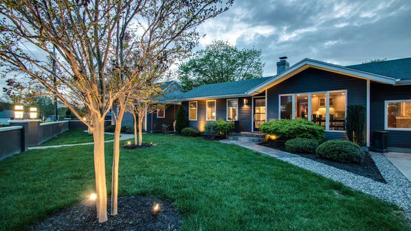 A modern house with a well-maintained lawn, a large tree, and a driveway leading to the entrance.