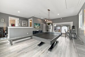 A spacious room with a ping pong table, a bench, and a dining area with chairs.
