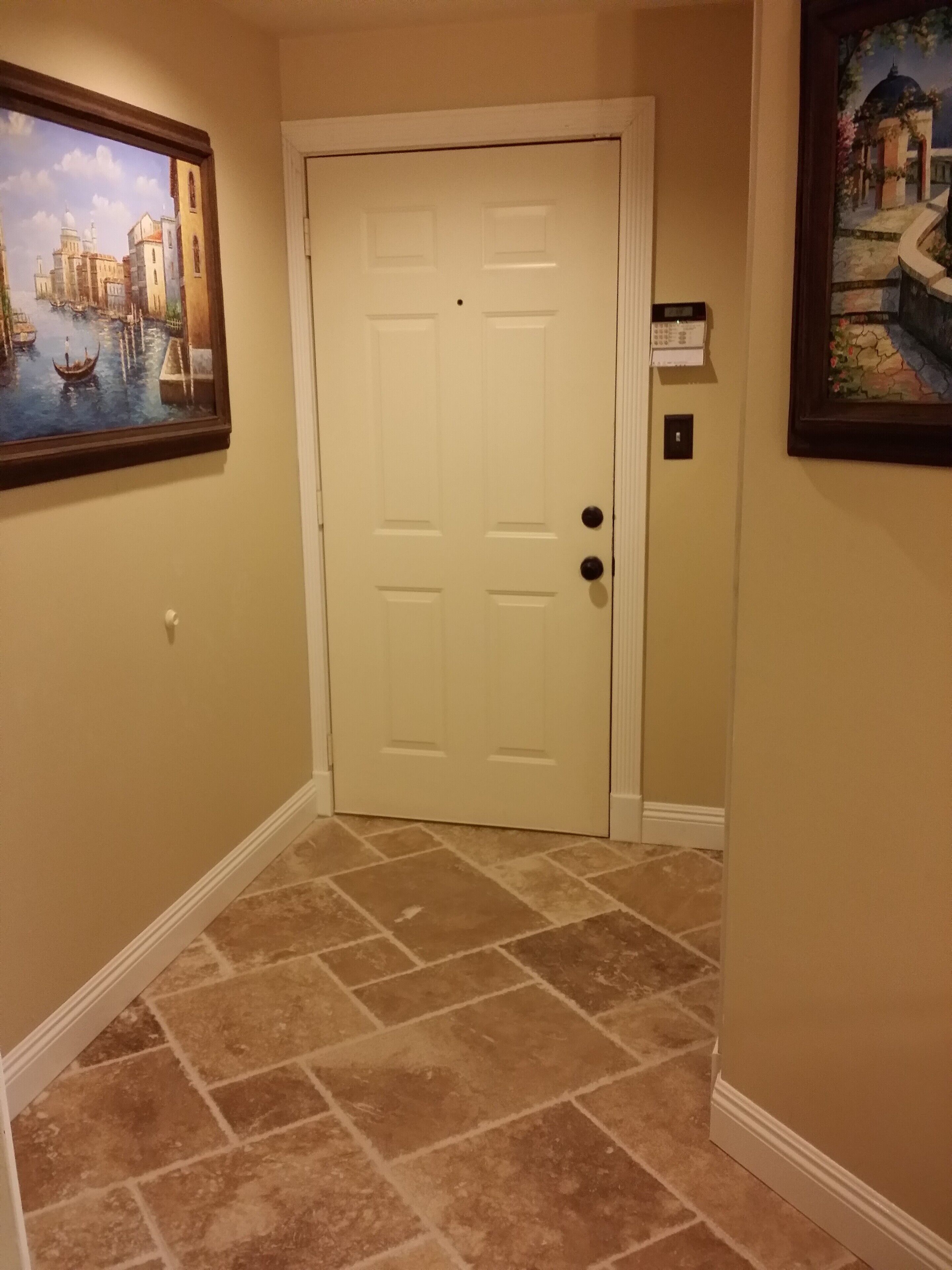 A hallway with a white door, a painting of a cityscape, and a tiled floor.