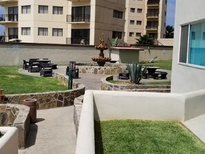 Um pátio com mesas ao ar livre, uma fonte e uma parede de pedra.