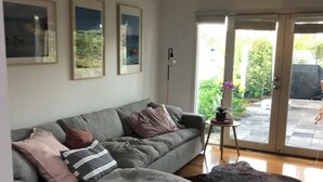 Uma sala de estar com um sofá cinza, um tapete de couro preto e quadros nas paredes.