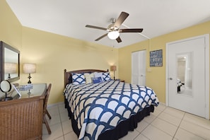 Une chambre à coucher comprenant un lit, un bureau, une chaise, un ventilateur de plafond et une porte.