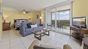 Ein geräumiges Wohnzimmer mit einer Couch, einem Couchtisch, einem Fernseher und einem Balkon mit Blick.