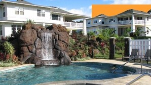Une piscine agrémentée d’une cascade, entourée d’une clôture et de palmiers.