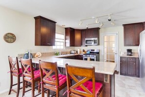 A kitchen with dark wooden cabinets, a central island with bar stools, a microwave, stove, and a refrigerator.