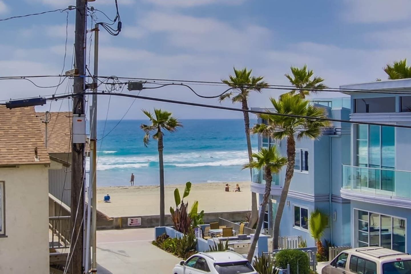 A coastal view with a beach, palm trees, and a building with large windows.