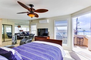 A hotel room with a bed, a desk, a television, a ceiling fan, and a balcony with a view of the ocean.