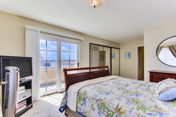 Habitación de hotel con cama, televisor, calefacción, armario y puerta corrediza de vidrio que da a un balcón.